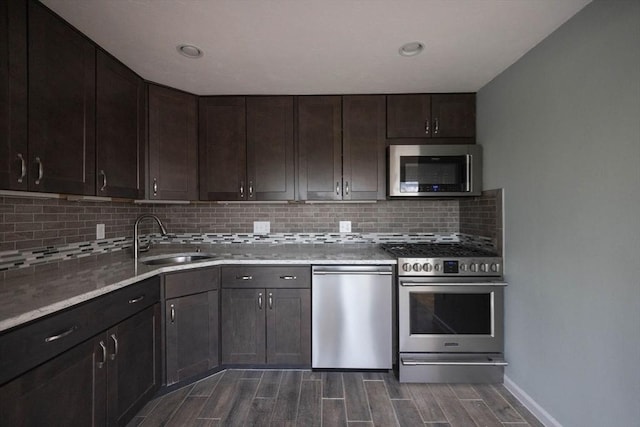 kitchen featuring wood finish floors, a sink, stainless steel appliances, dark brown cabinetry, and backsplash