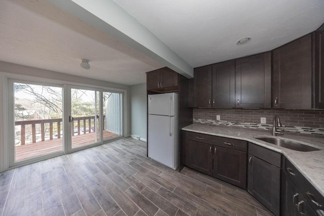 kitchen with tasteful backsplash, dark brown cabinets, freestanding refrigerator, and a sink