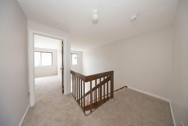 hall featuring an upstairs landing, light carpet, and baseboards