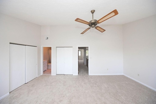 unfurnished bedroom with light colored carpet, multiple closets, ensuite bathroom, and baseboards