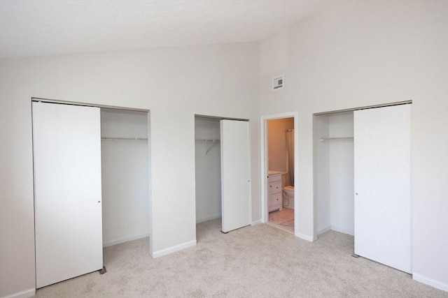 unfurnished bedroom with baseboards, visible vents, two closets, and light carpet