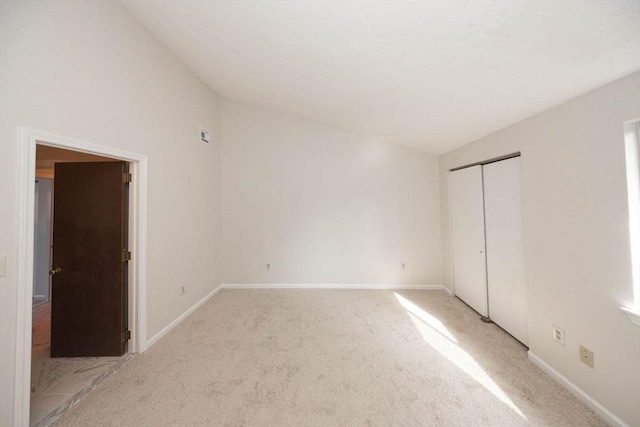 unfurnished bedroom featuring baseboards, light carpet, lofted ceiling, and a closet