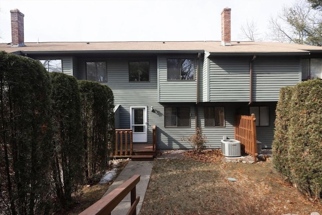 rear view of house with central air condition unit and a chimney