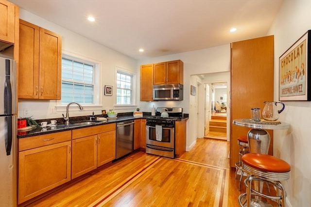 kitchen featuring appliances with stainless steel finishes, light wood-type flooring, a sink, brown cabinets, and recessed lighting