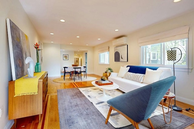 living area featuring a wall mounted air conditioner, light wood-type flooring, baseboards, and recessed lighting