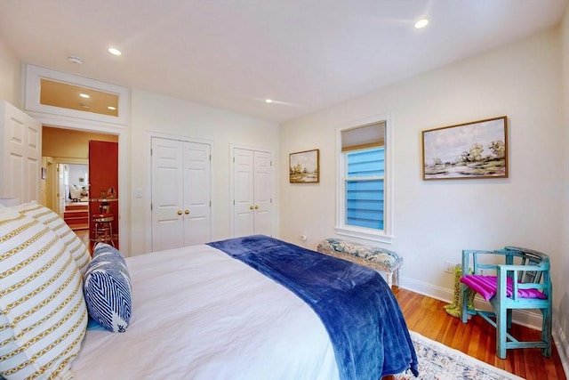 bedroom with two closets, wood finished floors, recessed lighting, and baseboards