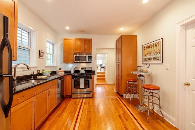 kitchen featuring stainless steel appliances, light wood-type flooring, brown cabinets, a sink, and recessed lighting