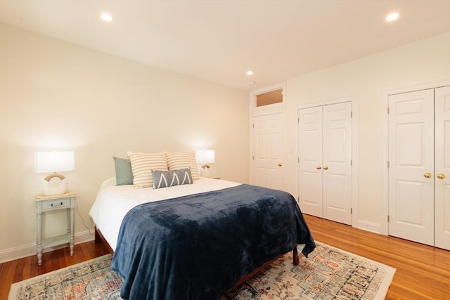 bedroom with two closets, light wood finished floors, recessed lighting, and baseboards