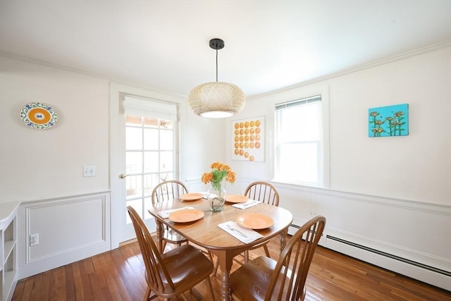 dining space with ornamental molding, wainscoting, hardwood / wood-style flooring, a baseboard radiator, and a decorative wall
