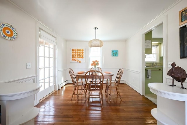 dining area with ornamental molding, wood-type flooring, wainscoting, baseboard heating, and a decorative wall