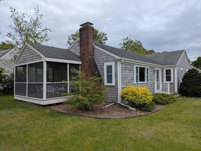rear view of property featuring a sunroom, a yard, roof with shingles, and a chimney