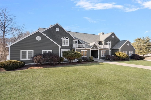 shingle-style home featuring a balcony, a chimney, and a front yard