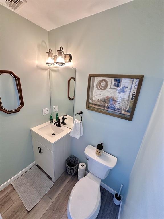 bathroom with toilet, wood finished floors, visible vents, and baseboards