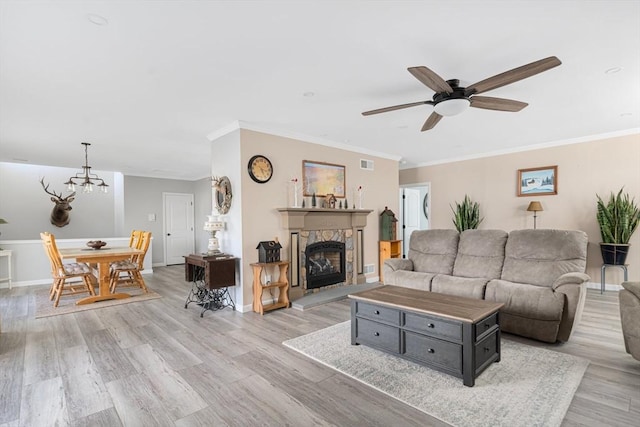 living area with a fireplace, ceiling fan with notable chandelier, light wood-type flooring, and baseboards