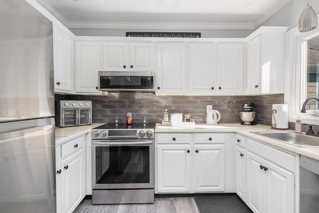 kitchen with wood finished floors, a sink, stainless steel appliances, light countertops, and white cabinets