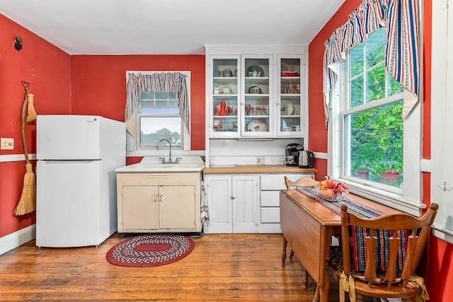 86 Glencoe St Unit 86, Boston, MA 02135 - kitchen with freestanding refrigerator, light countertops, a sink, light wood finished floors, and glass insert cabinets