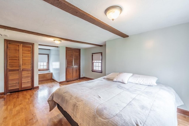 bedroom featuring visible vents, beamed ceiling, light wood-type flooring, baseboards, and two closets