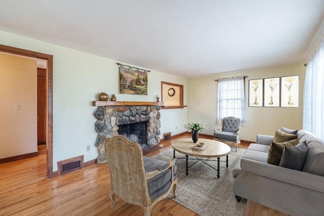 living room with a stone fireplace, light wood-style floors, visible vents, and baseboards
