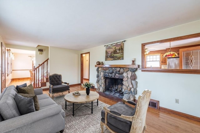 living room featuring stairway, wood finished floors, a stone fireplace, baseboards, and visible vents