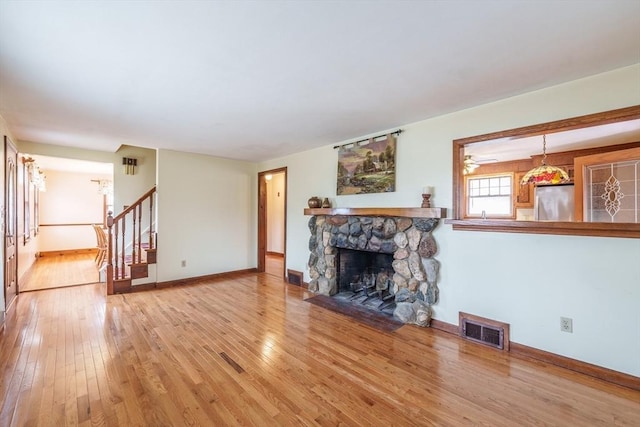 unfurnished living room featuring stairs, a stone fireplace, visible vents, and hardwood / wood-style floors