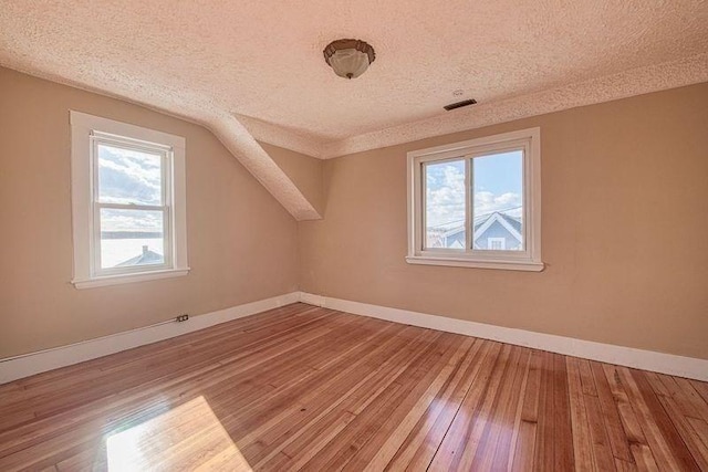 additional living space with hardwood / wood-style floors, vaulted ceiling, and a textured ceiling