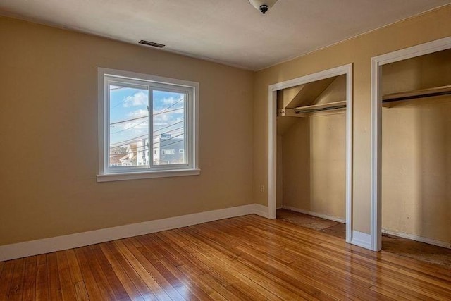 unfurnished bedroom featuring multiple closets and light hardwood / wood-style flooring