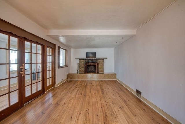 unfurnished living room featuring french doors, a stone fireplace, and light hardwood / wood-style flooring