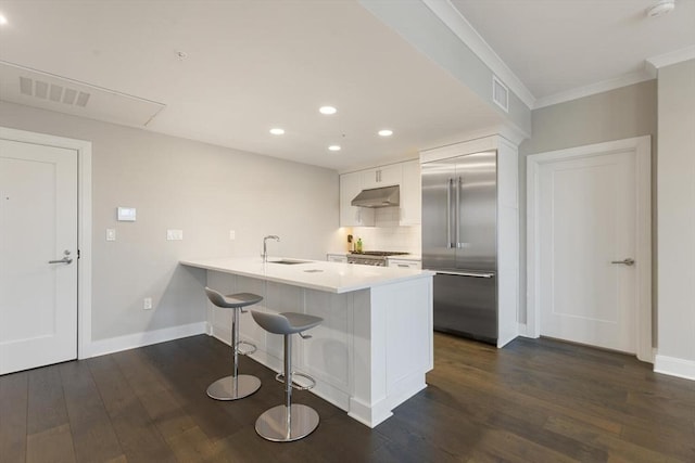 kitchen with under cabinet range hood, visible vents, built in fridge, and a sink