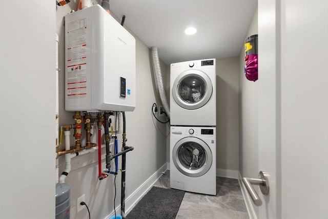 laundry area with tankless water heater, stacked washer / drying machine, baseboards, and laundry area