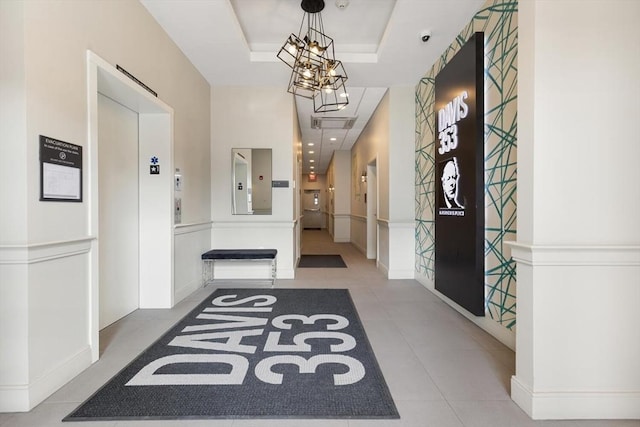 corridor with a tray ceiling, elevator, an inviting chandelier, and tile patterned flooring