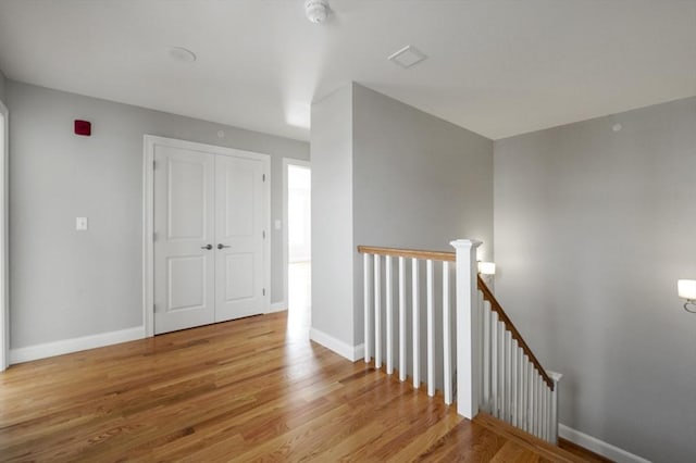 hallway with an upstairs landing, baseboards, and wood finished floors