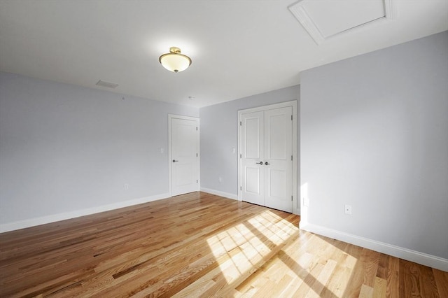 unfurnished room featuring visible vents, baseboards, attic access, and wood finished floors