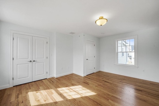 unfurnished bedroom with a closet, visible vents, baseboards, and wood finished floors