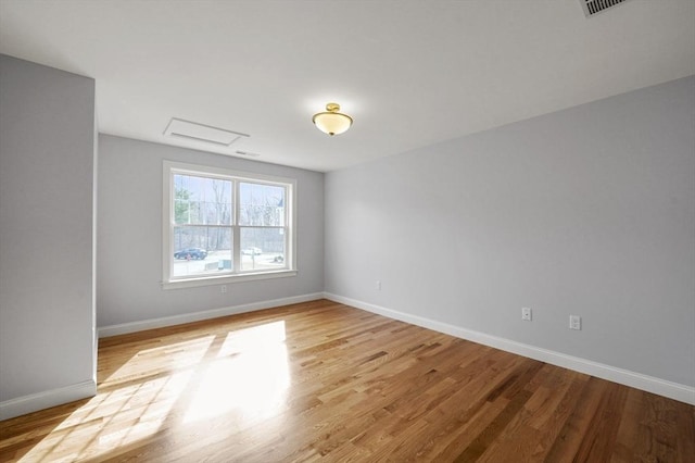 unfurnished room with light wood-type flooring, baseboards, and attic access