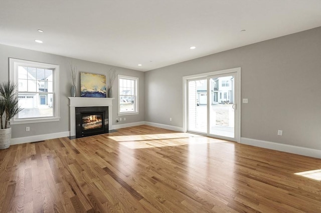 unfurnished living room featuring a fireplace with flush hearth, wood finished floors, and baseboards