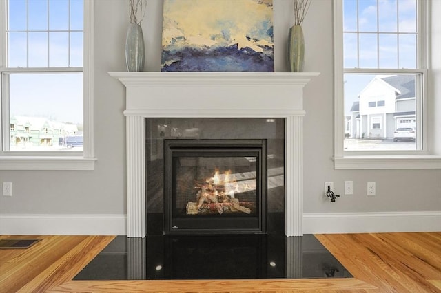 interior details featuring baseboards, a fireplace with flush hearth, visible vents, and wood finished floors