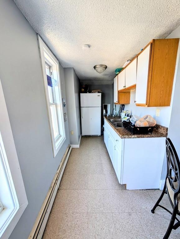 kitchen with a baseboard heating unit, light floors, freestanding refrigerator, white cabinetry, and a sink