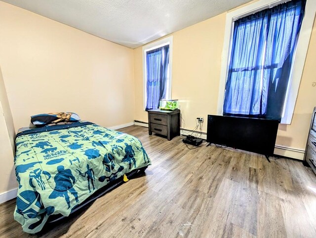 bedroom featuring baseboard heating, a textured ceiling, baseboards, and wood finished floors