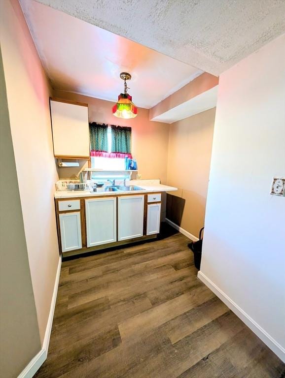 kitchen with dark wood-style floors, baseboards, a sink, hanging light fixtures, and a textured ceiling