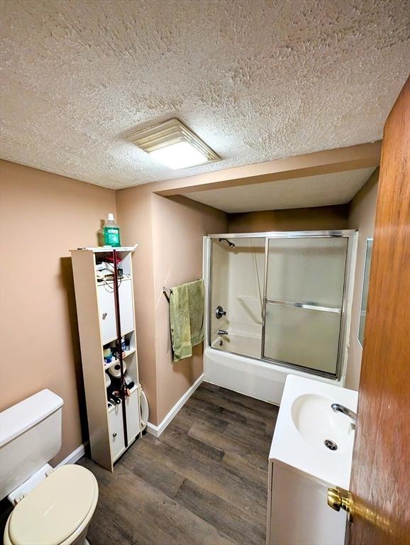 full bath featuring vanity, wood finished floors, a textured ceiling, toilet, and combined bath / shower with glass door