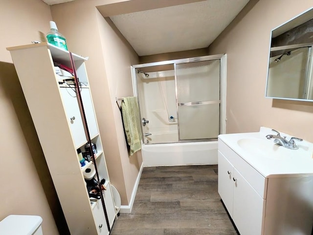 bathroom featuring baseboards, toilet, wood finished floors, enclosed tub / shower combo, and vanity