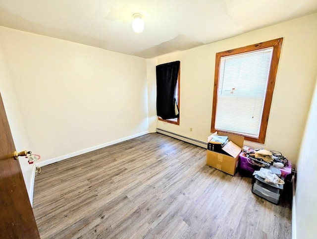 empty room featuring a baseboard heating unit, baseboards, and wood finished floors