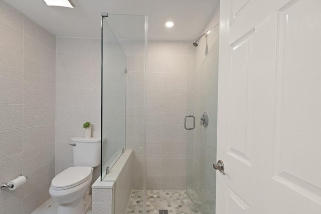 bathroom featuring toilet, tile walls, and a shower with shower door