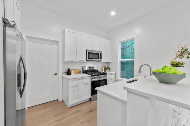 kitchen with light hardwood / wood-style flooring, appliances with stainless steel finishes, kitchen peninsula, sink, and white cabinets