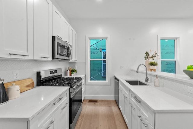 kitchen with light wood-type flooring, appliances with stainless steel finishes, white cabinetry, and sink