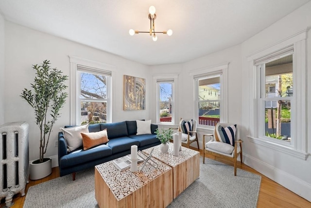 living room featuring baseboards, a notable chandelier, radiator heating unit, and light wood finished floors