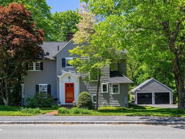 view of front of property with an outbuilding, a detached garage, a chimney, and roof with shingles