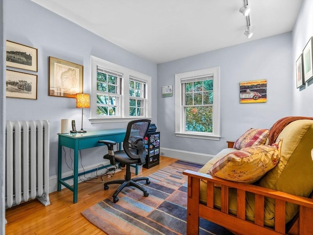 home office featuring radiator heating unit, wood finished floors, baseboards, and rail lighting