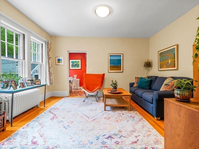 living area with radiator heating unit, light wood-type flooring, and baseboards
