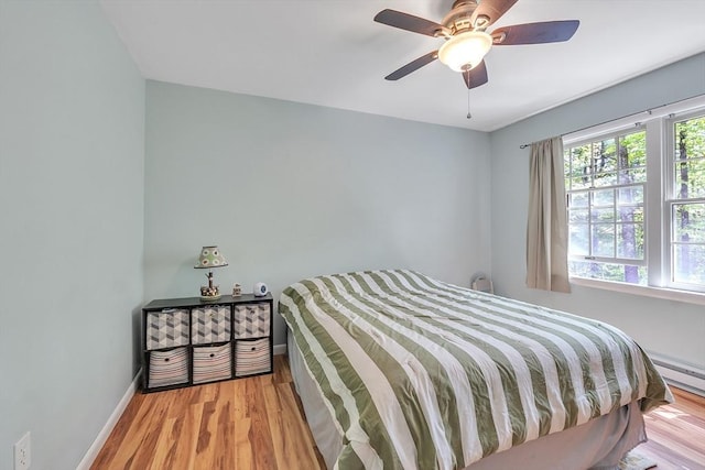 bedroom featuring wood finished floors, baseboards, ceiling fan, and a baseboard heating unit